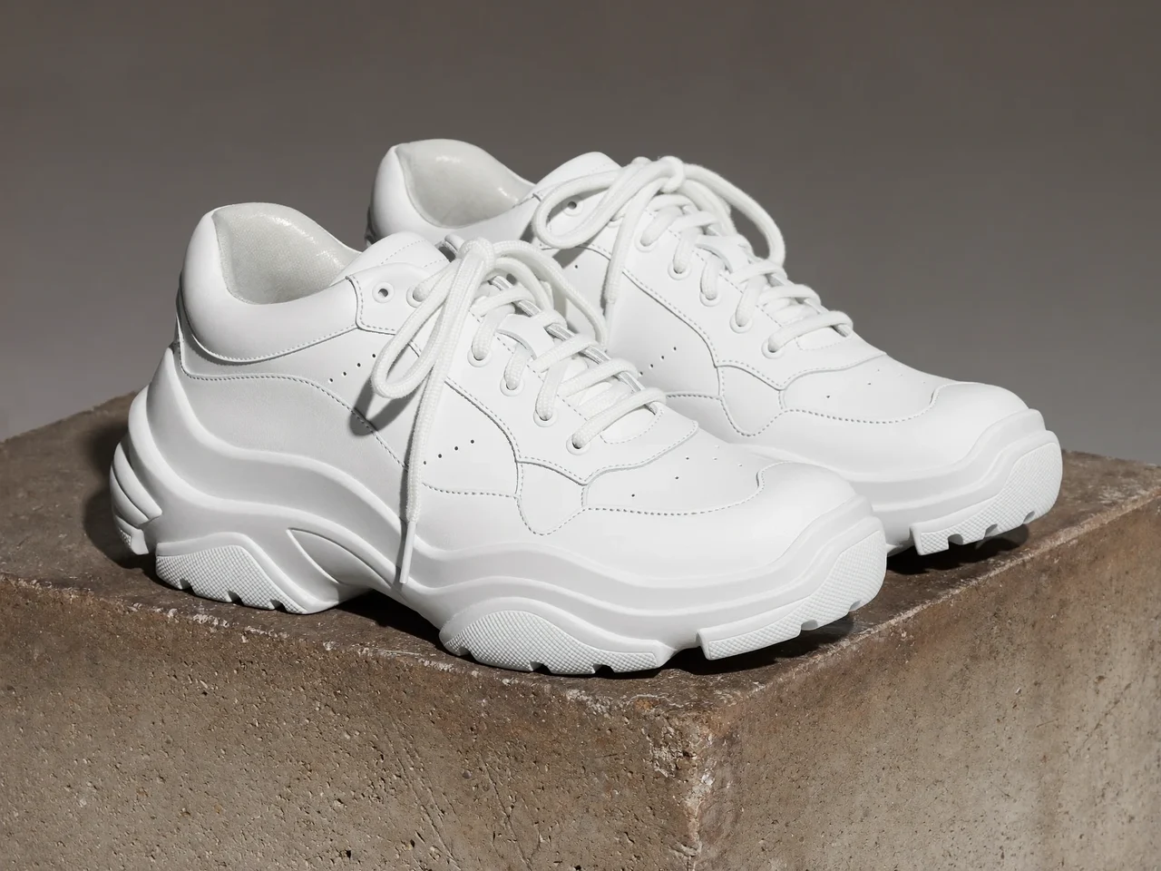 Hvide læder-sneakers med tyk sål på en ru betonblok